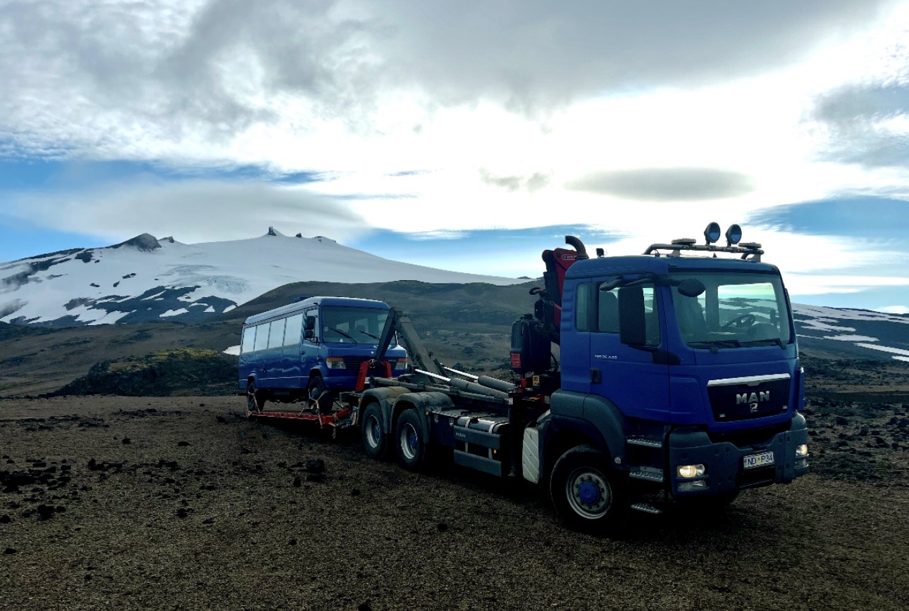 MAN transport truck with a minibus on a trailer in mountain terrain